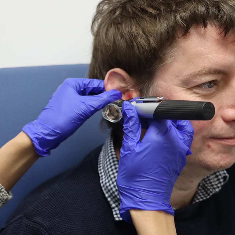 Audiologist examining a patient's ear with an otoscope, focusing on the ear canal and eardrum.
