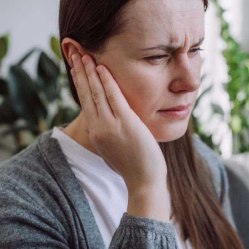 A woman appears to be in pain, touching her ear.