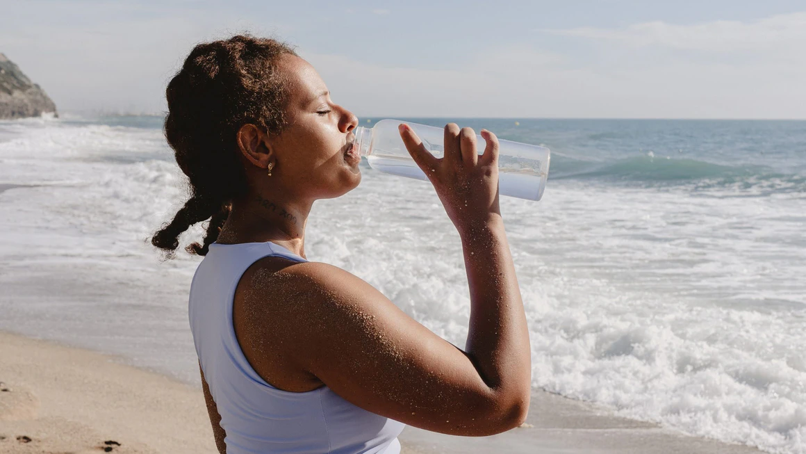 Woman driking water from a bottle by the beach.