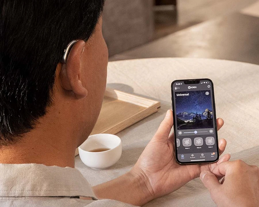A man wearing a hearing aid and using Widex app on his phone.