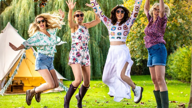 Four women jumping in the air in front of a tent.