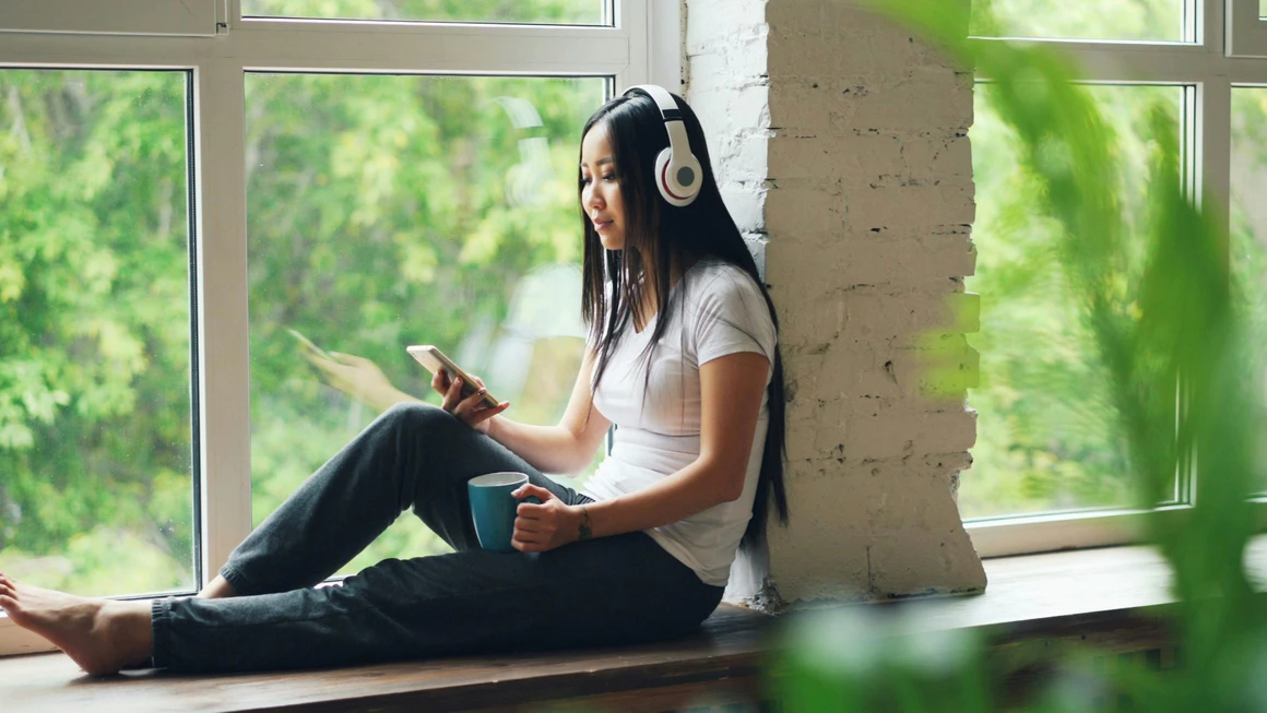 Woman relaxing with headphones by sunny window.