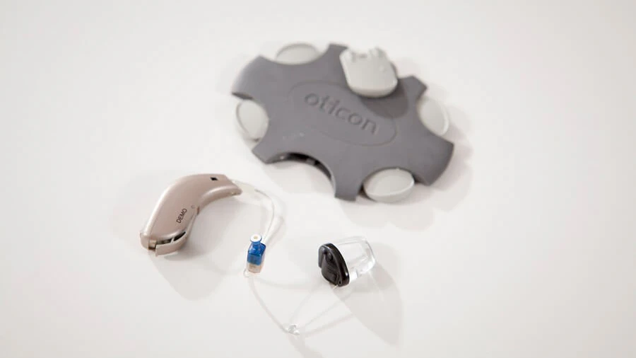 Oticon 'No Wax' wax guards next to a hearing aid.