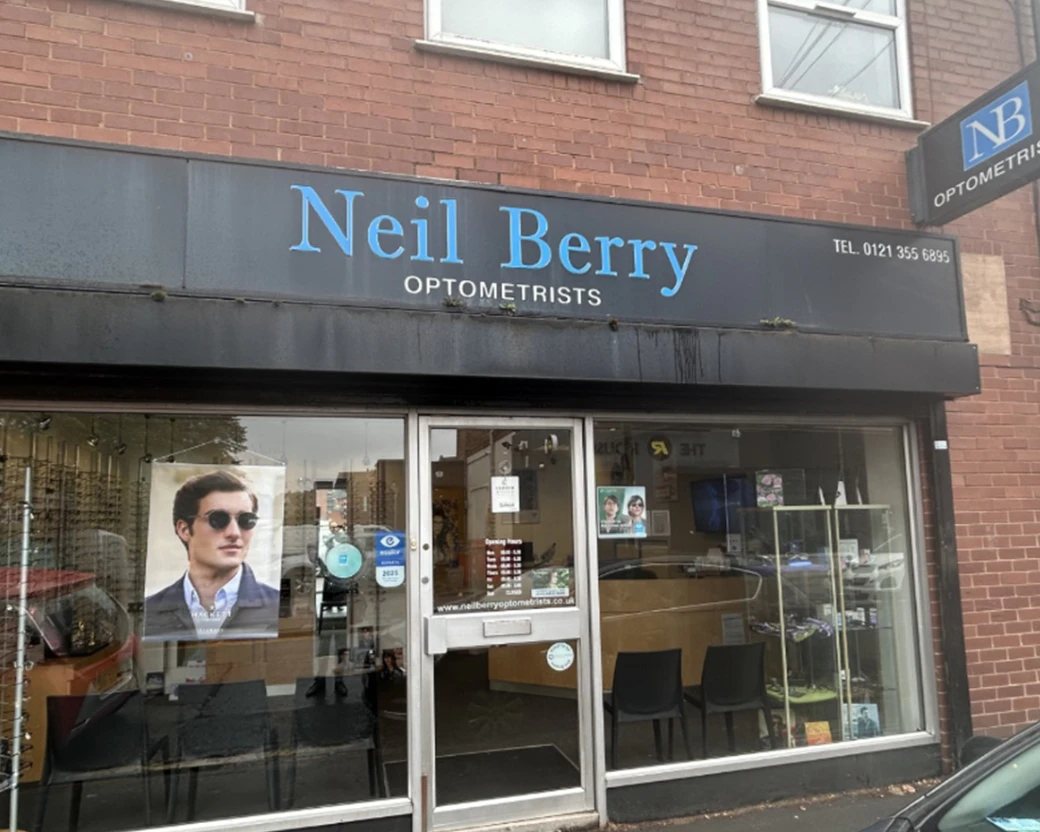 Neil Berry Optometrists, outside the practice with a black sign and frame displays inside