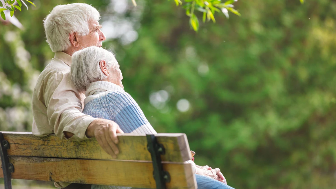 An elderly couple sitting together on a park bench.