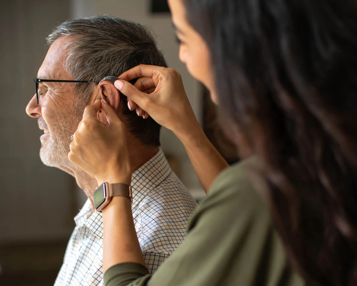 Side view of an audiologist fitting a hearing aid in a patient's ear.